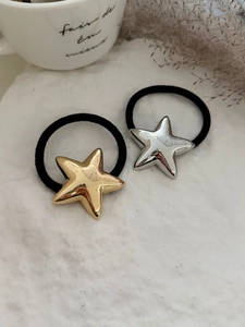 Dettaglio degli elastici per capelli a stella in metallo oro e argento su sfondo bianco