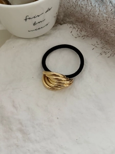 Dettaglio di un elastico per capelli nero con ciondolo metallico dorato lucido a più anelli