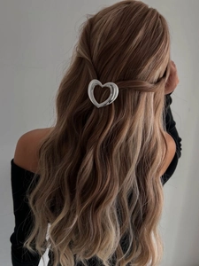 Pince à cheveux cœur évidé argentée portée sur de longs cheveux bruns ondulés