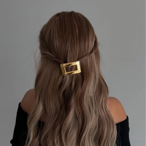 Barrette rectangulaire minimaliste en métal doré portée sur des longs cheveux ondulés