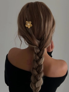 Detail of golden flower hair pin with pearl on model's hair against grey wall