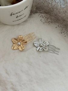 Detail of gold and silver flower hair pins with pearls on a textured white background