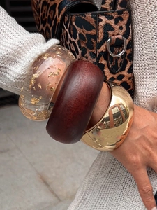 Detailed shot of stacked wide bangles in gold, resin with gold foil, and matte wood finish