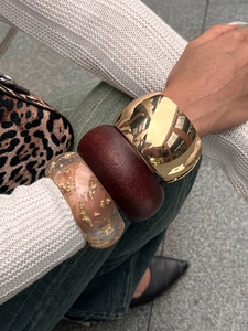 Close-up of stacked wide bangles featuring gold metal, wood texture, and gold foil resin
