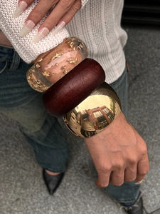 Close-up of stacked chunky bracelets in gold metal, wood, and gold-leaf resin materials