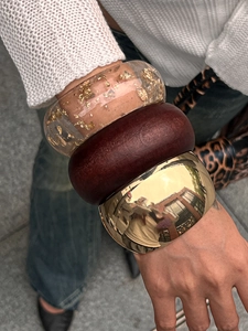 Stacked set featuring chunky gold metal, dark wood, and resin bangles on a model's wrist