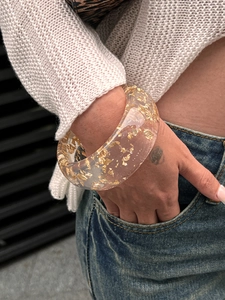 Macro shot of wide transparent resin bangle with embedded gold foil flakes for women