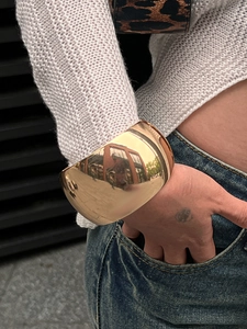 Close-up of wide gold cuff bracelet featuring a mirror-polished finish on model's wrist