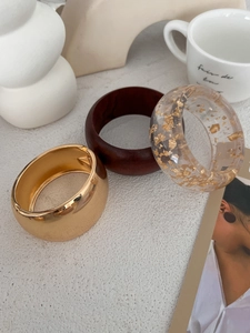 Detailed trio of wide bangles in polished gold metal, wood, and gold leaf resin