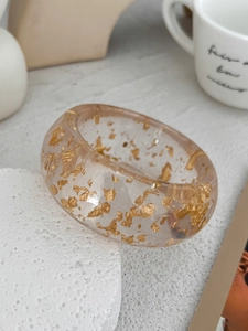 Detail of wide resin ring with gold foil flakes on white mineral stone stand