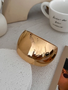 Close-up of a wide gold-plated open bangle with mirror polish on a beige background