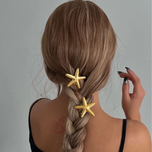 Pair of textured golden starfish hair pins worn on braided hair with summer style