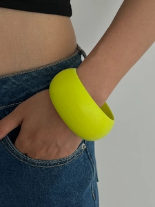 Nahaufnahme eines breiten neongelben Holzarmreifs am Handgelenk eines Models