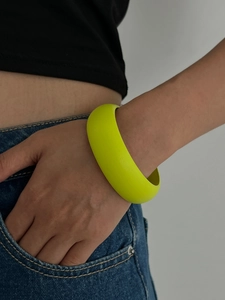 Nahaufnahme eines breiten fluoreszierenden grünen Armreifs am Handgelenk mit Denim
