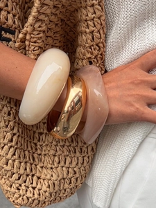 Close-up of set of thick gold, cream, and pink resin bangles worn on a model's wrist
