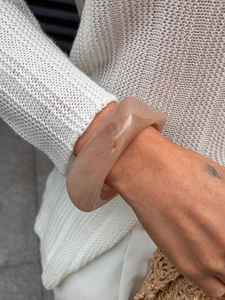 Close-up of thick beige resin bangle with marble texture on model wearing knit sweater