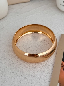 Macro view of gold high-polished chunky bangle with a sleek mirror finish on white background