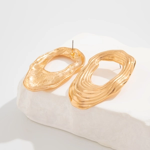 Detail von unregelmäßigen goldenen Ohrringen mit Wellentextur auf Steinsockel