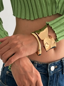 Dettaglio di un bracciale a polsino dorato oversize con superfici concave irregolari