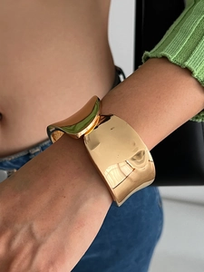 Dettaglio macro del bracciale rigido dorato largo con design concavo e finitura lucida