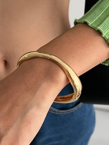 Dettaglio di un ampio bracciale concavo in oro lucido indossato con maglia verde