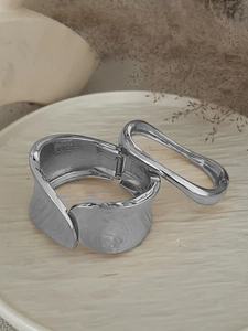 Dettaglio del polsino ondulato argento e bracciale minimalista su piatto ceramica