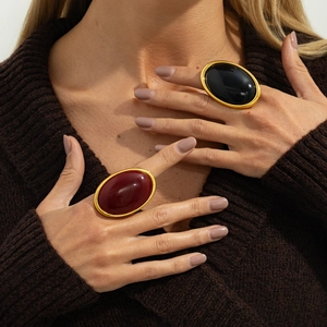 Detailed view of oversized oval burgundy and black gemstone rings with gold metal finish