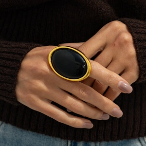 Detail of chunky gold-tone oval ring with large black resin stone on knit texture