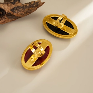 Detail view of retro gold-plated oval rings with red and black resin inlay on beige surface