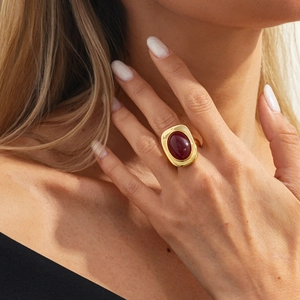Close-up of a vintage gold-plated ring featuring a large oval deep red gemstone on a finger
