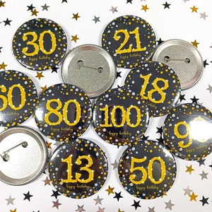 Detailed close-up of black and gold 58mm tinplate birthday badges with sparkling numbers