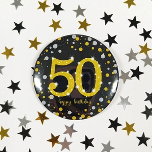 Close-up of a black and gold 50th birthday badge with festive star confetti background