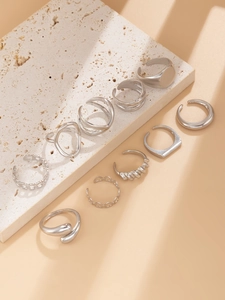 Set of nine minimalist silver geometric rings displayed on a textured stone surface