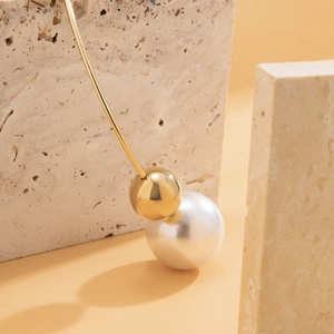 Macro shot of minimalist gold drop earring with pearl detail on beige travertine stone