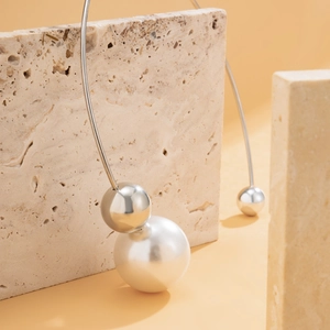 Close-up of pearl and silver sphere choker displayed on beige travertine stone texture