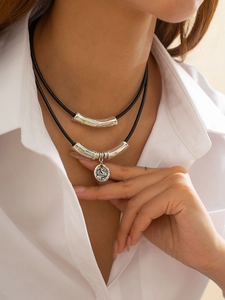 Detail view of a double-layered necklace with curved silver tubes and a relief coin pendant