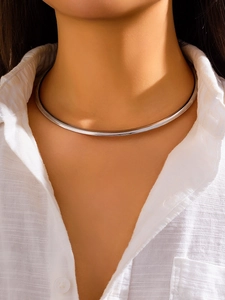 Gros plan d'un collier ras du cou argenté porté avec une chemise en lin blanc