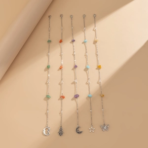 Detail of five silver chains with colorful natural stones and bohemian charms on beige background