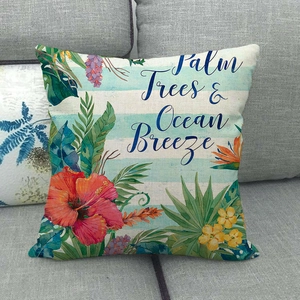 Détail de la taie d'oreiller en lin avec palmiers fleurs d'hibiscus et texte sur un canapé