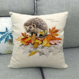 Détail d'une housse de coussin en lin avec hérisson parmi des feuilles d'automne