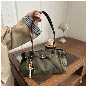 Dettaglio della borsa tote in tela verde scuro con manici in pelle marrone e ciondolo