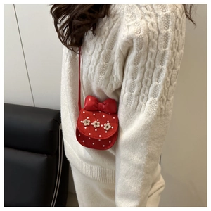 Sac bandoulière enfant rouge à pois blancs avec nœud fleuri porté par un modèle