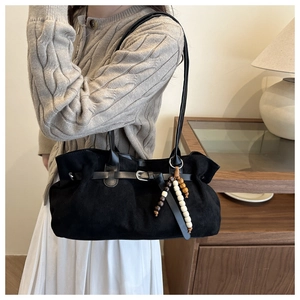 Dettaglio borsa tote in pelle scamosciata nera con fibbia decorativa e ciondolo in legno