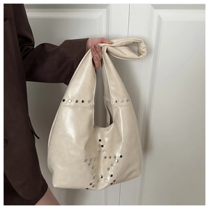 Close-up of creamy white hobo bag with silver star-shaped metal rivets and knotted handle
