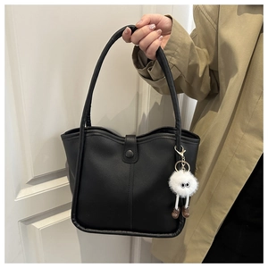 Détail d'un sac seau en cuir PU brillant noir avec un porte-clé monstre en peluche blanc