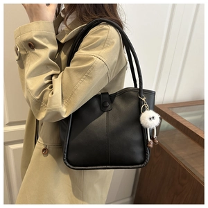 Detalle del bolso tote negro mate con correa de hombro y accesorio de amuleto de peluche blanco