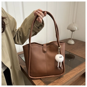 Détail d'un sac cabas marron foncé avec texture mate et pendentif en peluche blanche