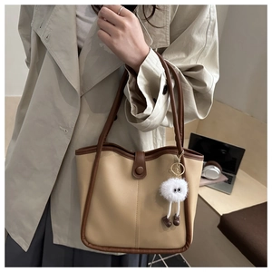 Détail d'un sac cabas beige avec bordure marron et charm en peluche sur un bureau