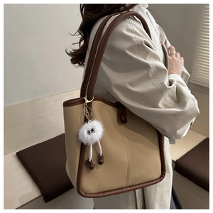 Détail latéral du sac cabas kaki et marron avec un pendentif peluche de monstre