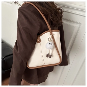 Détail d'un sac cabas beige et marron avec breloque en peluche sur un mannequin en blazer